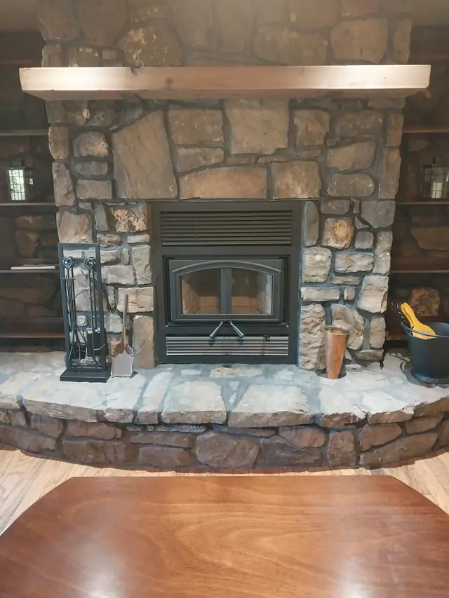 Finished stone fireplace with an insert, a wood mantel and a stone hearth