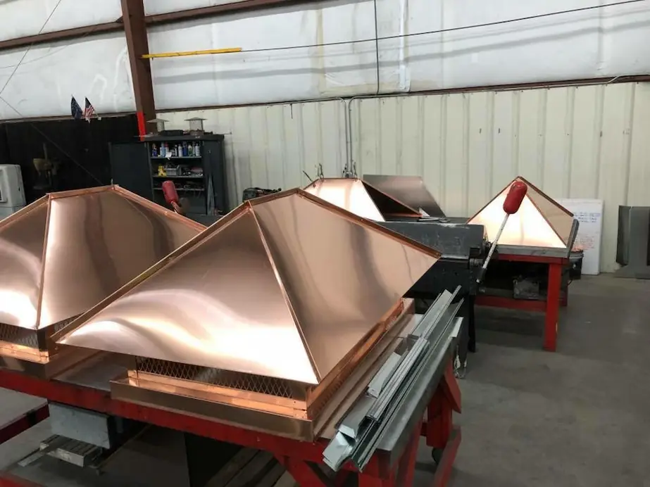 Copper chimney caps lined up on workshop benches